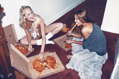 two women sitting on the floor eating pizza