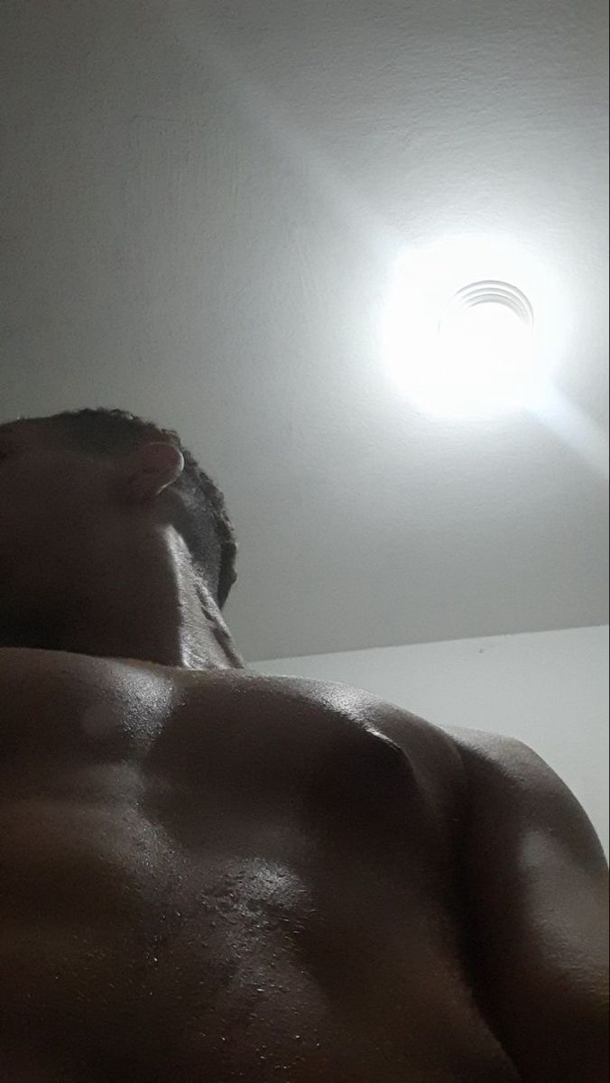 a man with no shirt standing in front of a ceiling light and looking up at the ceiling