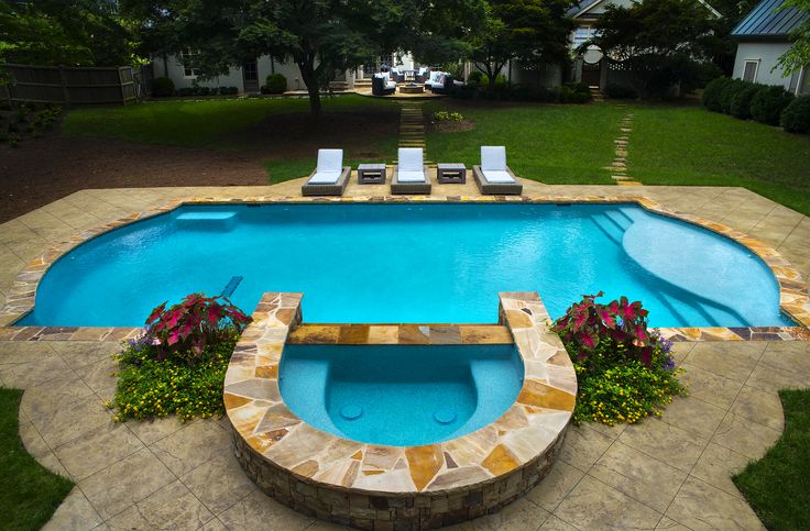 an empty swimming pool surrounded by lawn chairs and flowers in the foreground, next to a stone patio with chaise lounges