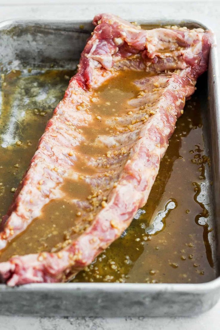 a piece of meat sitting on top of a pan filled with sauce and seasoning