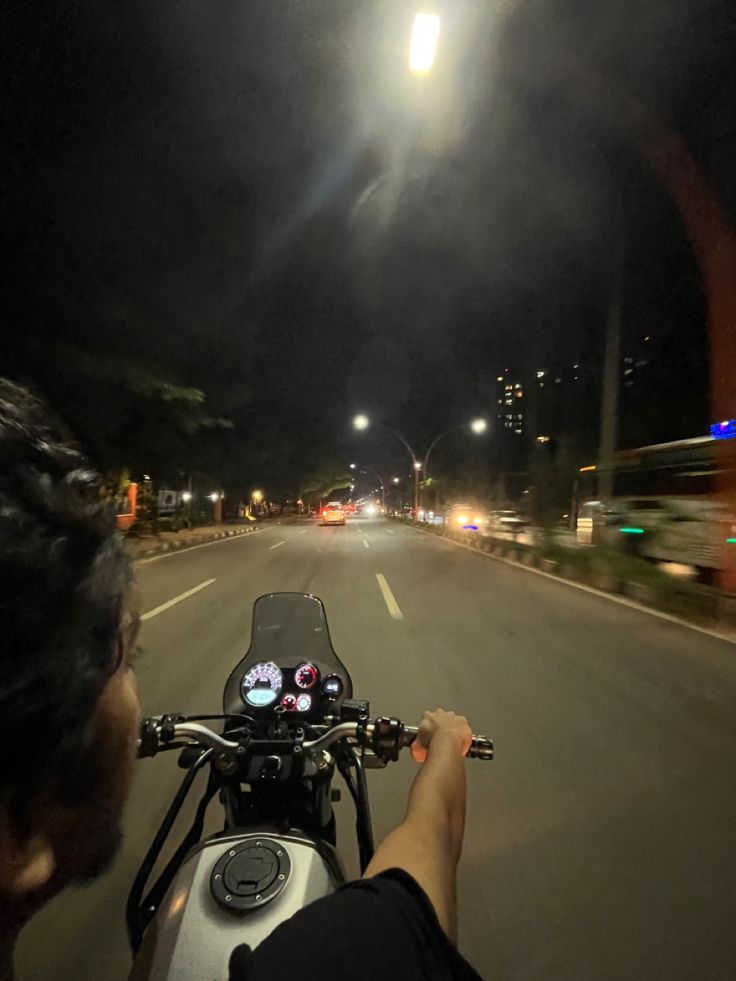 a person on a motorcycle driving down the road at night with street lights in the background