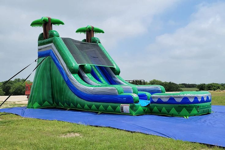 an inflatable water slide with two palm trees on top and blue tarp