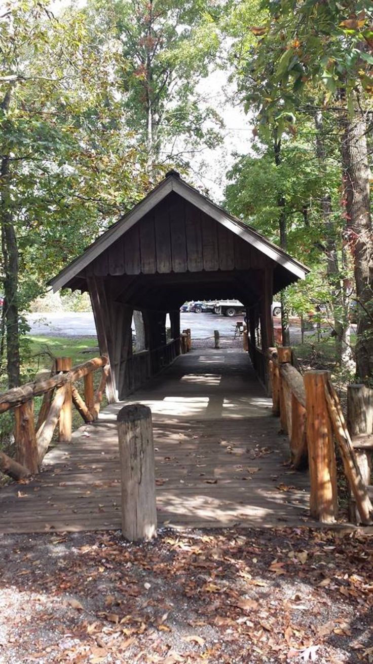 a wooden covered bridge in the woods with trees around it and cars parked on the other side