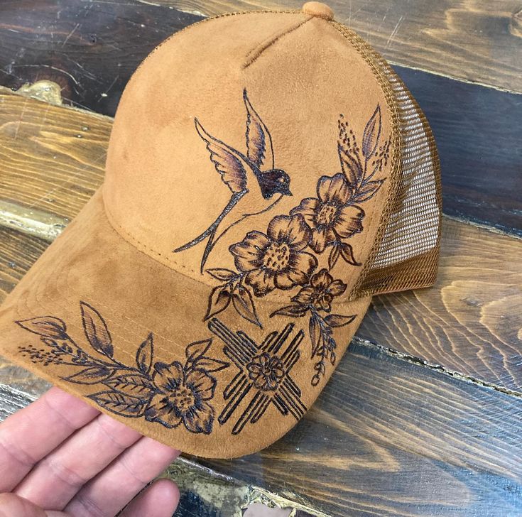 a person holding up a brown hat with floral designs on the front and side of it