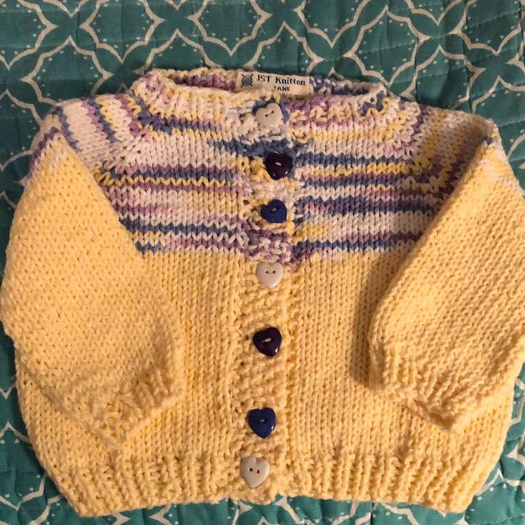 a yellow knitted sweater with buttons on the front and back, sitting on a bed