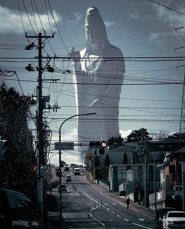 a large statue is in the middle of an urban area with power lines above it