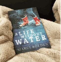 a book sitting on top of a white blanket next to a black chair with red boots