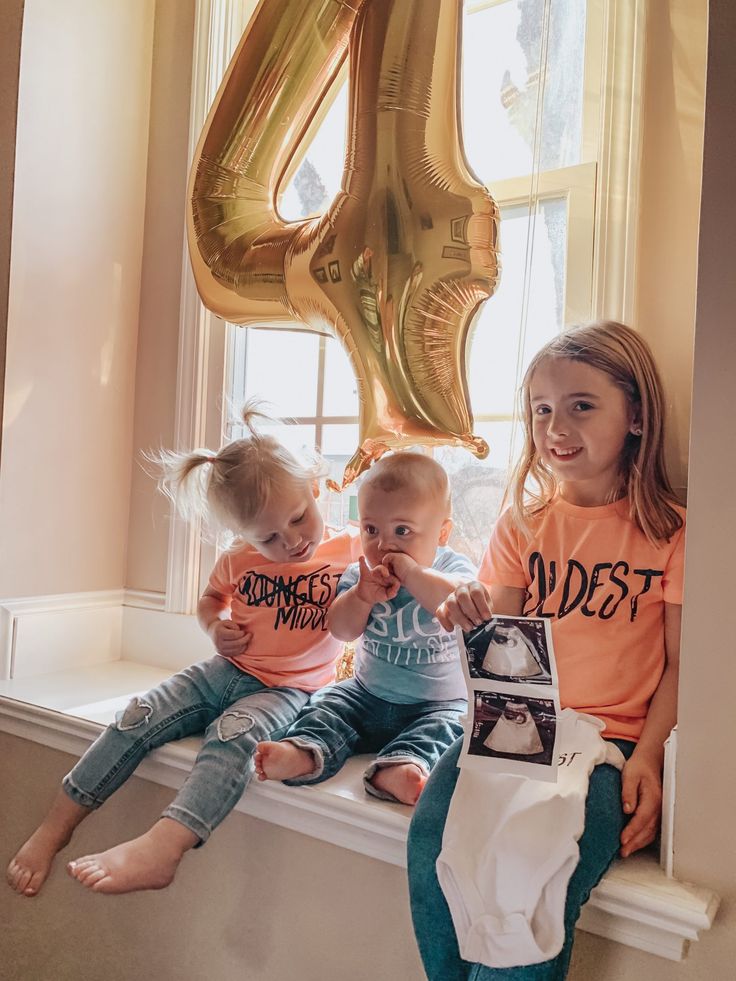 three young children sitting on a window sill in front of a number four balloon