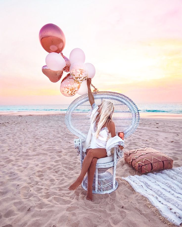 a woman sitting in a chair on the beach with balloons