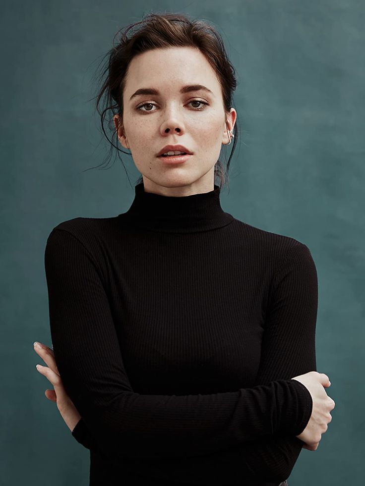 a woman in a black turtle neck top posing for the camera with her arms crossed