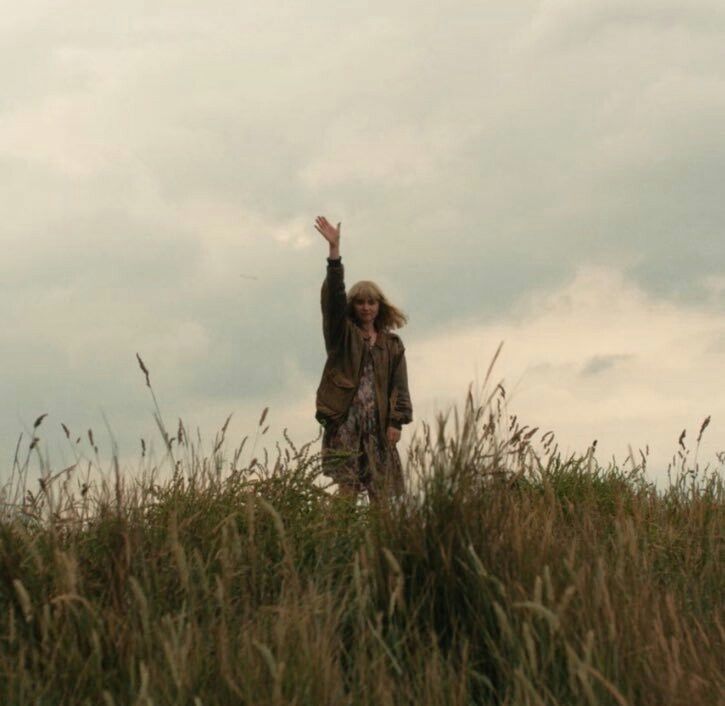 a woman standing on top of a lush green field next to a kite flying in the sky