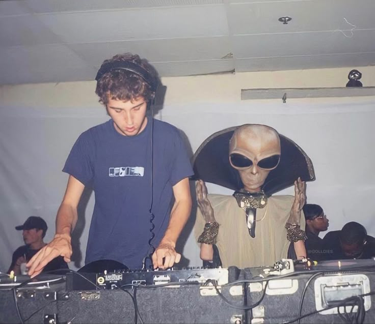 two men in alien costumes are djing at a party with headphones on and one man is wearing an alien costume