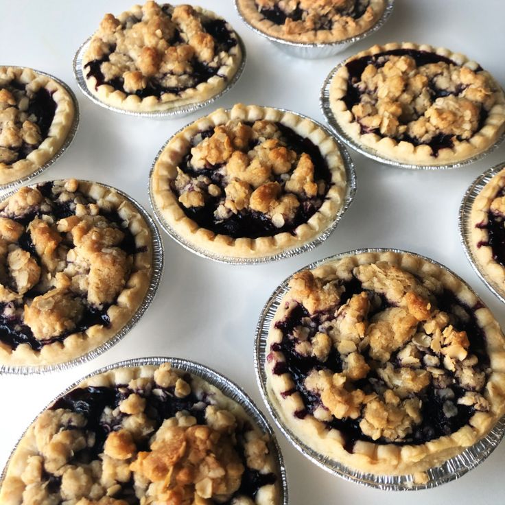 several pies with blueberries in them on a white counter top, ready to be eaten