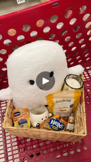 a stuffed animal sitting in a basket filled with snacks and other items on top of a red shopping cart