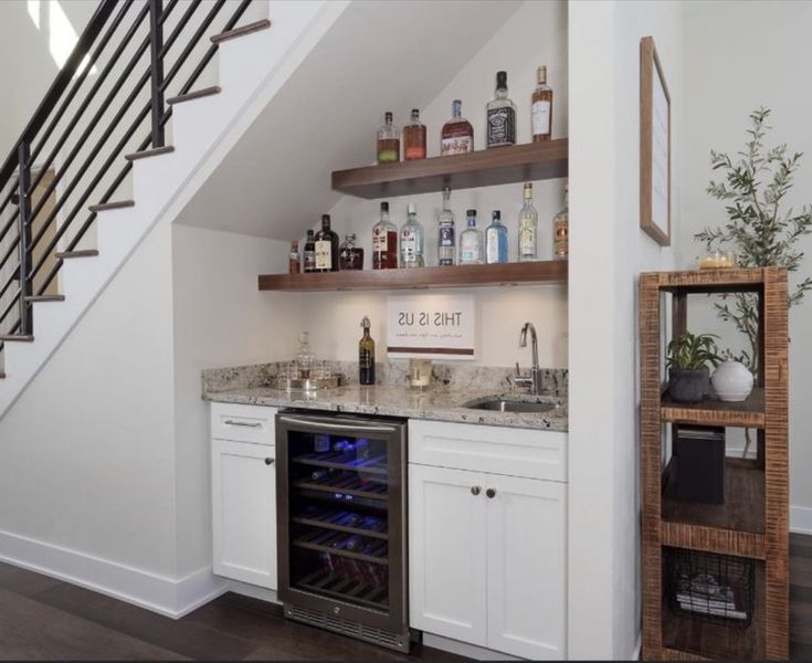 a kitchen with white cabinets and an under counter wine cooler next to the stairs that lead up to the second floor