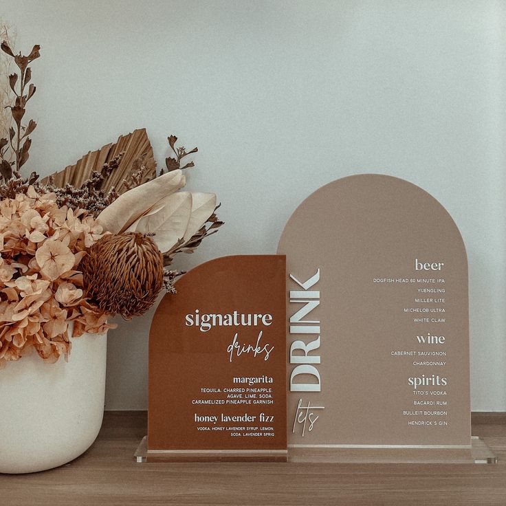 there is a vase with dried flowers next to a drink menu on the counter top