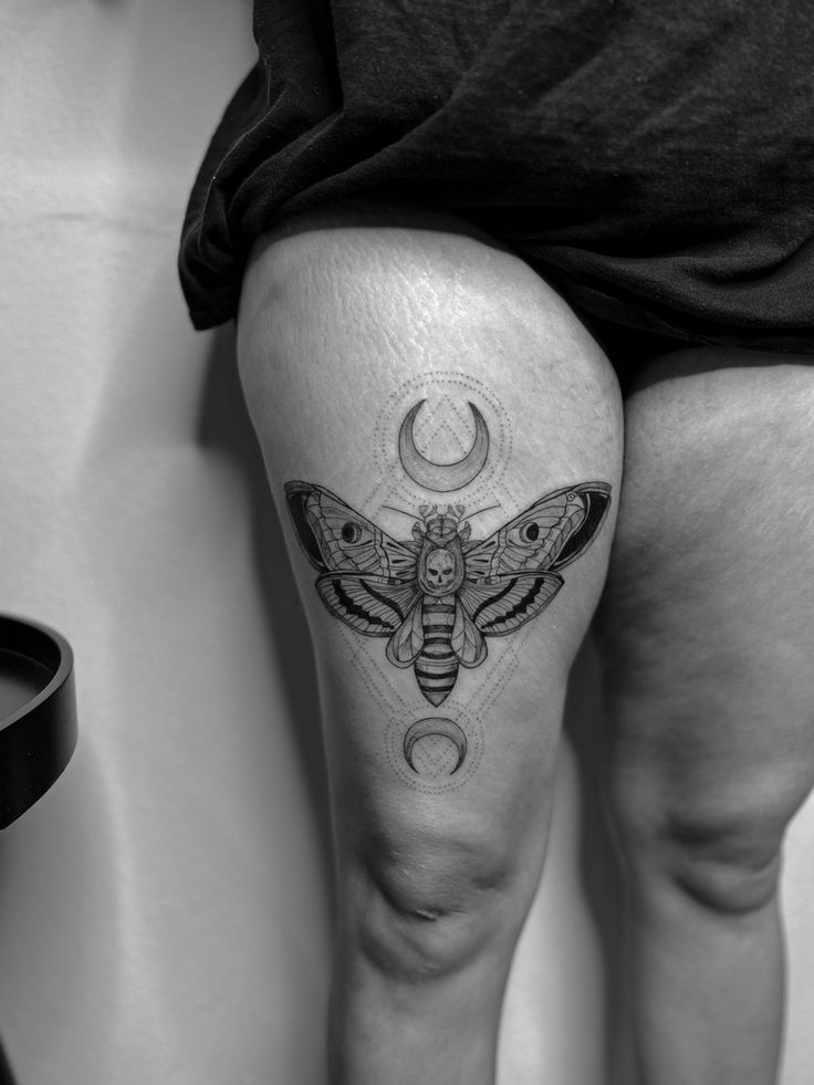 a woman's thigh with a moth and moon tattoo on her leg, in black and white