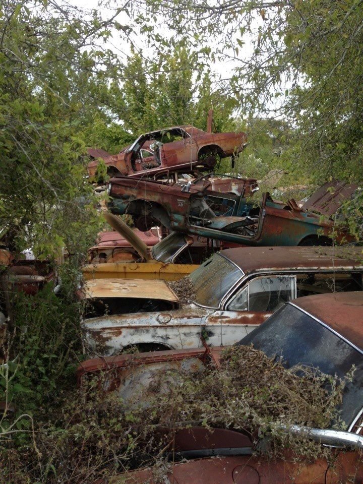 an old rusted out car sits in the middle of a field full of junk