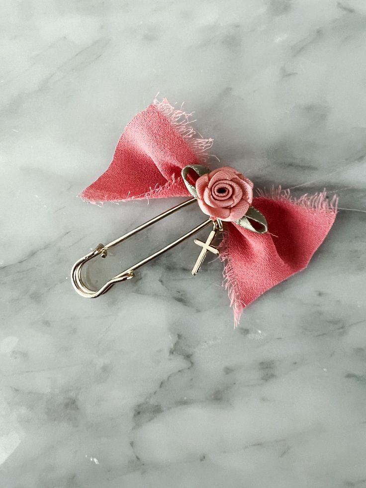 a pink bow with a rose on it is sitting on a marble surface and has two metal clips attached to it