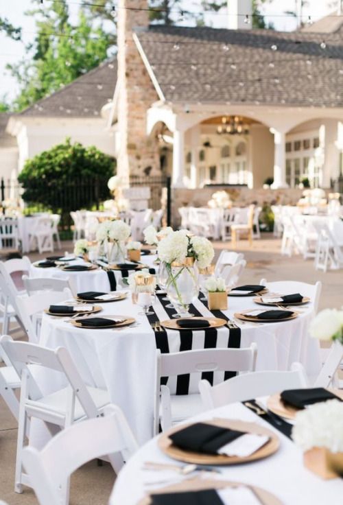 tables set up with black and white napkins for an outdoor wedding reception in front of a large house