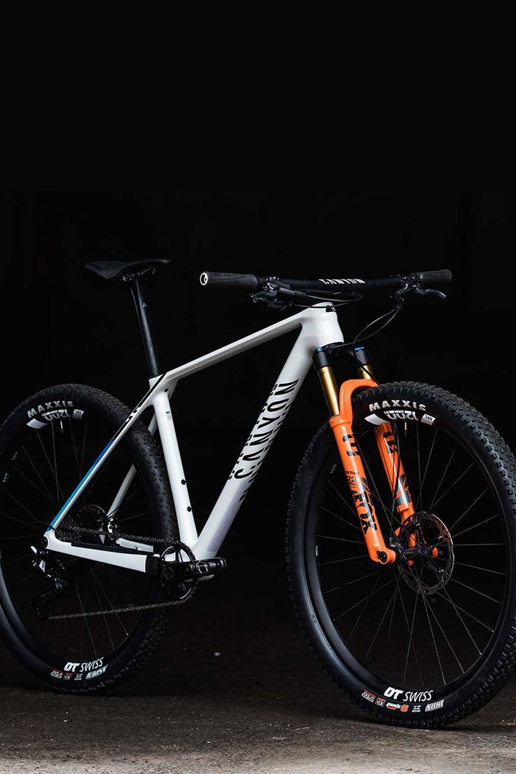 a white and orange bike parked in front of a black wall with no wheels on it