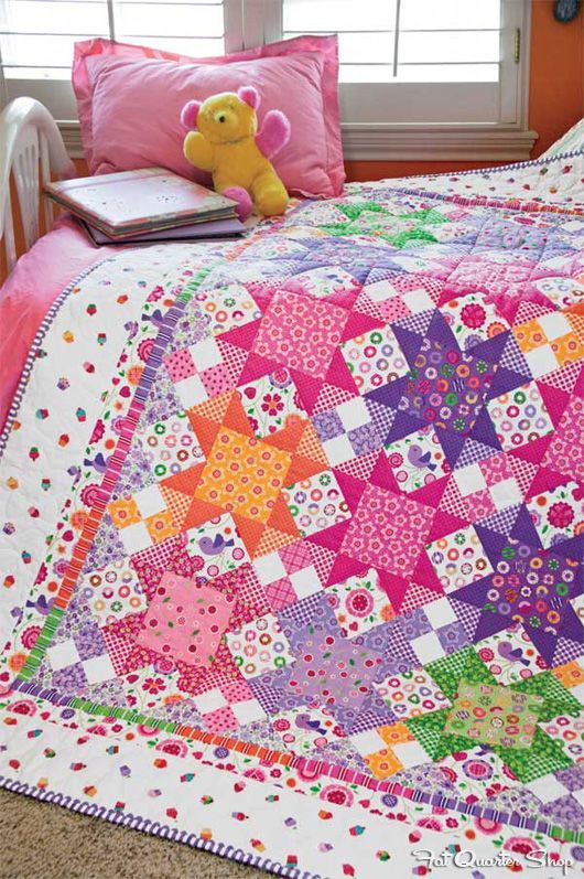 a bed with a colorful quilt on it and a teddy bear sitting next to it