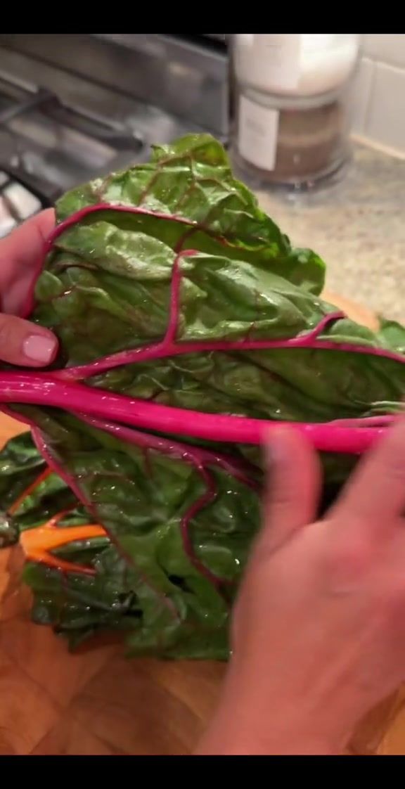 a person is cutting up some vegetables on a wooden board with red onions and green leafy greens