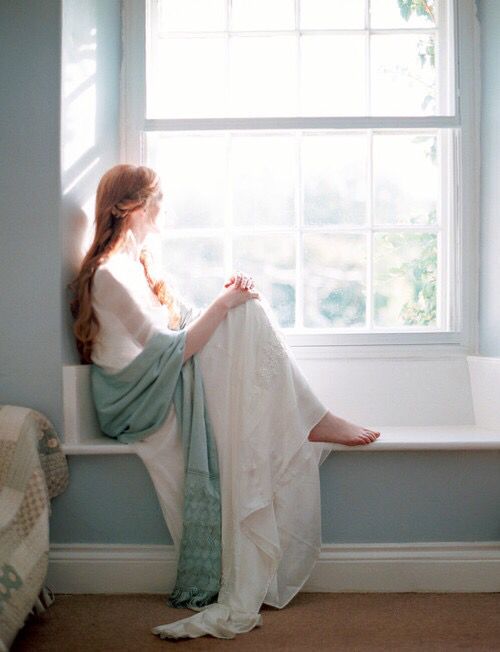 a woman sitting on a window sill looking out the window