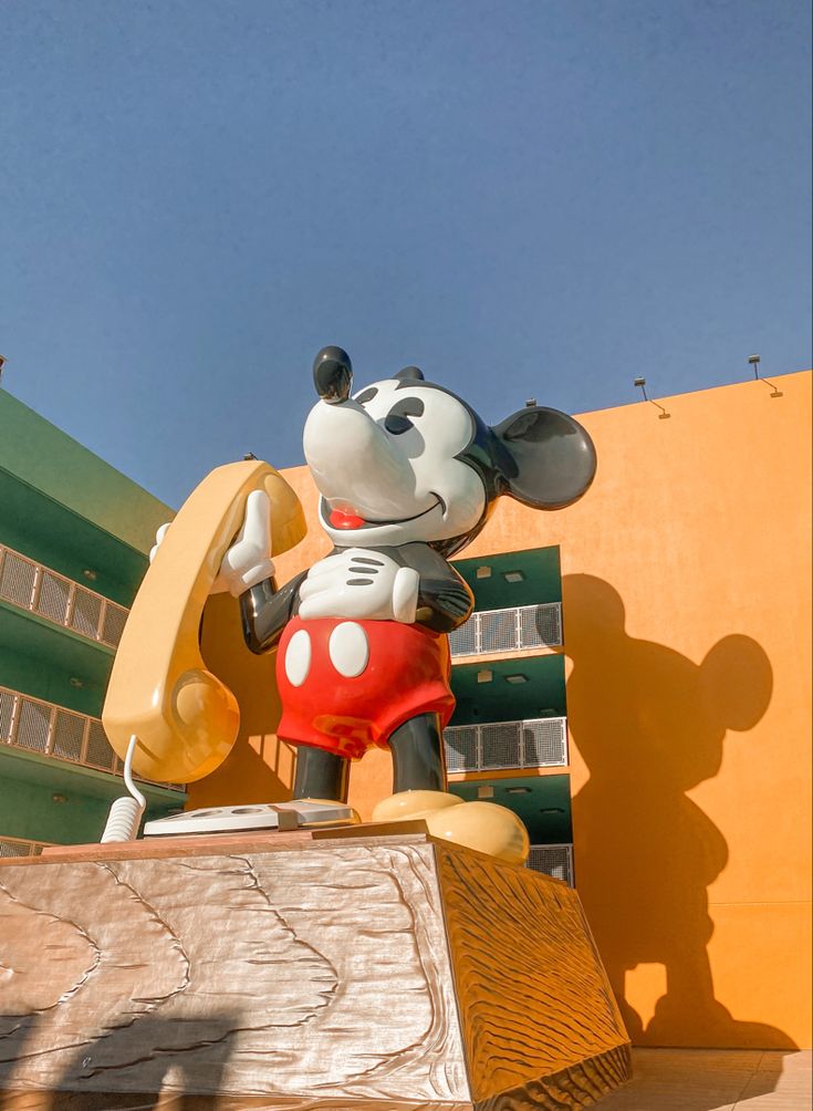 a statue of mickey mouse holding a hot dog in front of a building with yellow walls