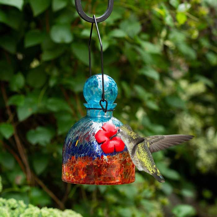 a colorful bird feeder with a hummingbird on it's side hanging from a tree