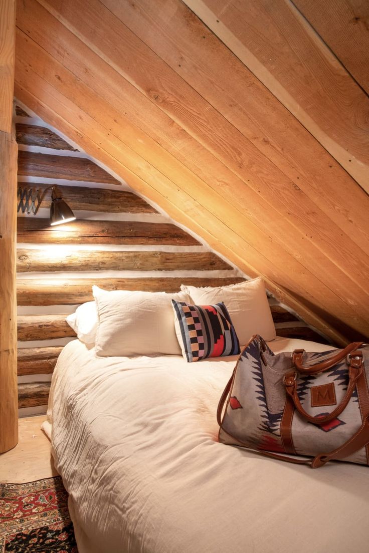 a bed with pillows and a purse on top of it in a room that is made out of wood