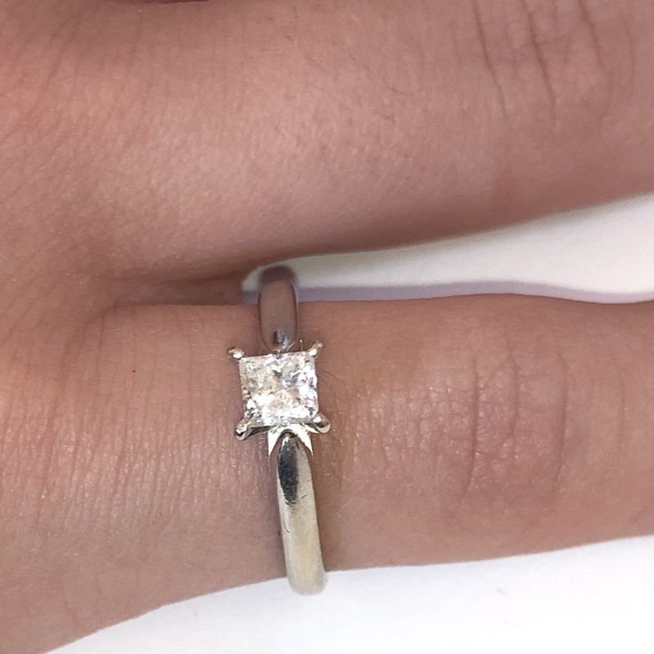 a woman's engagement ring with a princess cut diamond in the center on her finger