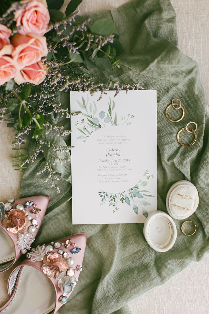 the wedding stationery is laid out with shoes, rings, and flowers on top