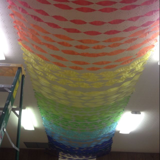 a large multicolored piece of art hanging from a ceiling in a room with ladders