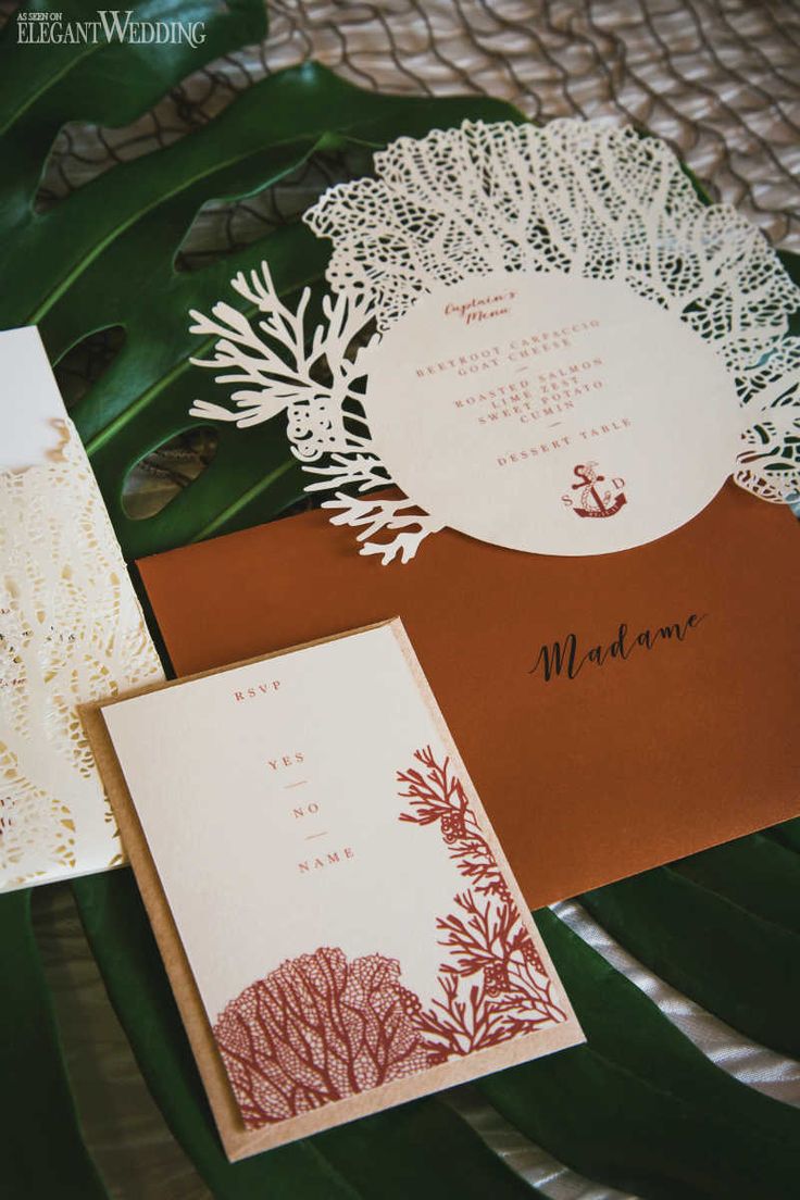 the wedding stationery is laid out on a leafy tablecloth with an anchor and coral design