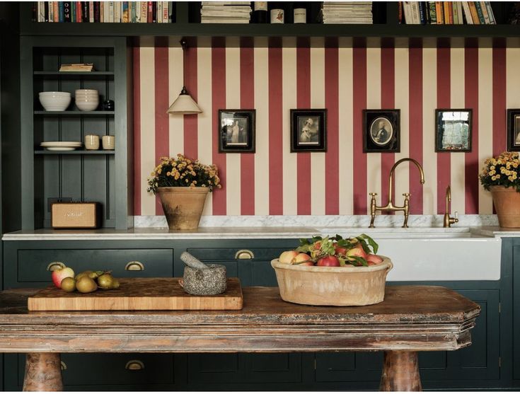 a kitchen with green cabinets and striped wallpaper on the walls, along with a wooden table topped with fruit