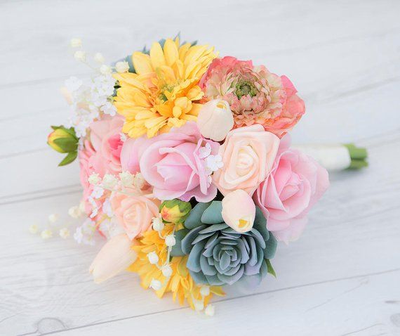 a bridal bouquet with pink, yellow and white flowers on a white table top