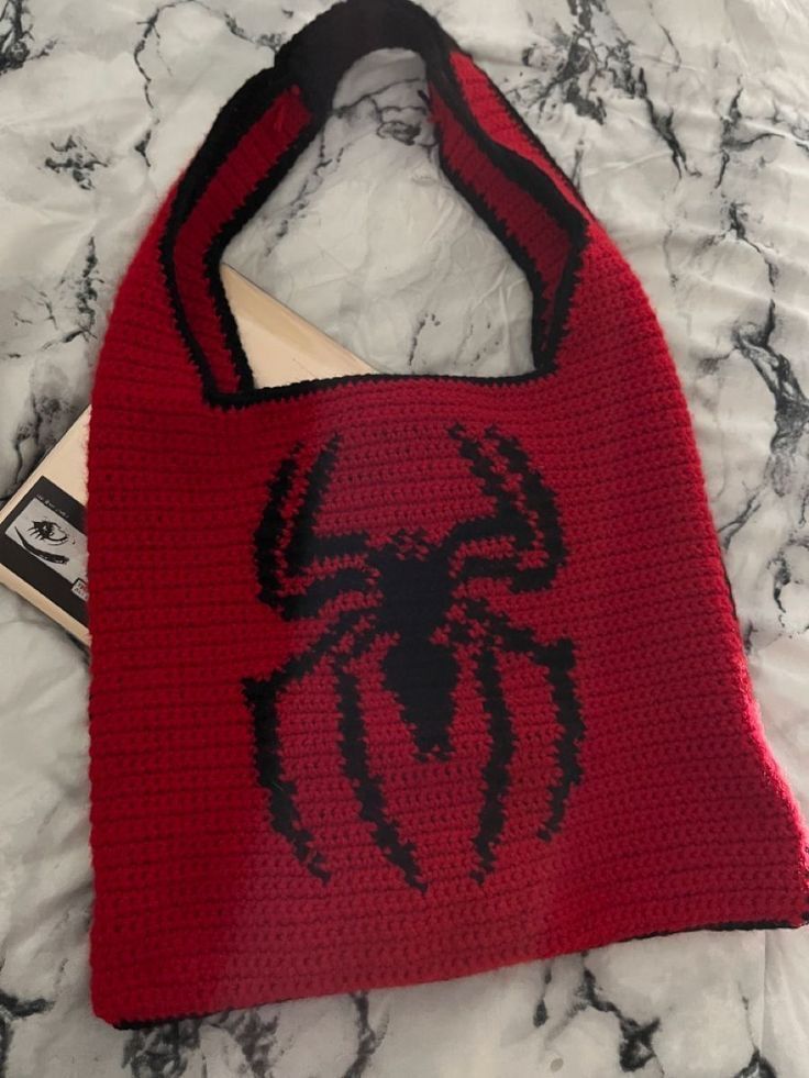 a red crocheted bag with a black spider logo on it sitting on a marble surface