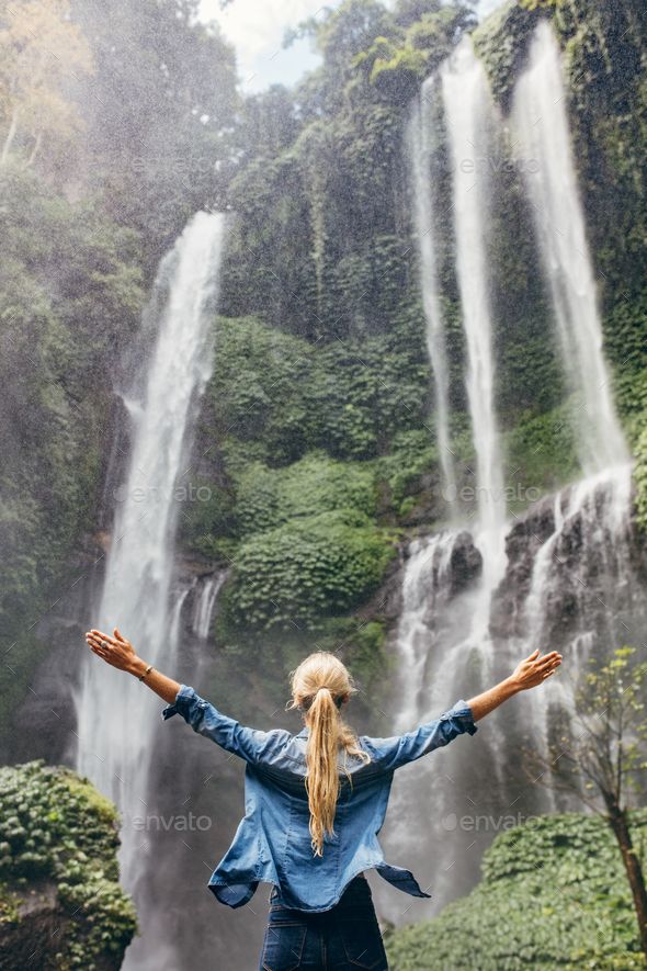 a woman standing in front of a waterfall with her arms spread wide out to the side