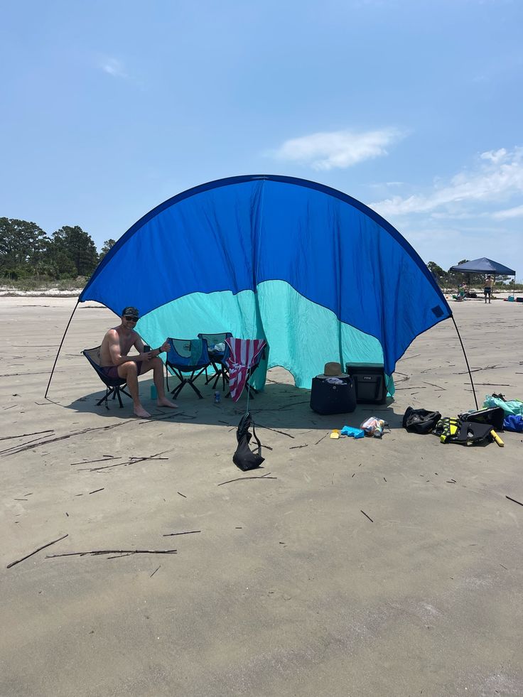 a man sitting under a blue and white tent on the beach