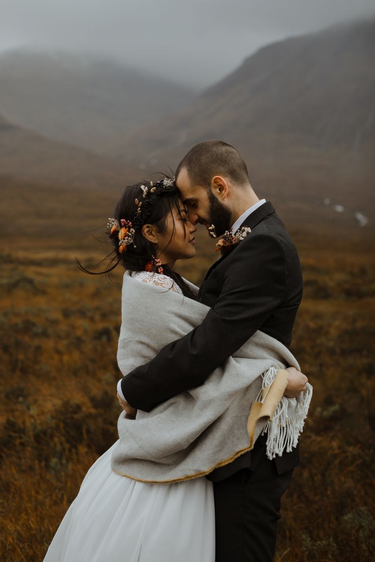 a bride and groom embrace in the mountains on their wedding day, while holding each other