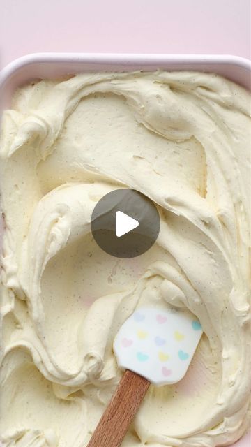 an ice cream in a white container with a wooden spoon on it and a pink background