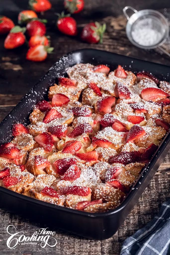 a pan filled with dessert covered in powdered sugar and strawberries on top of a wooden table