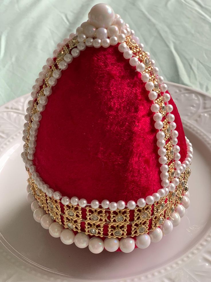 a white plate topped with a red and gold cake covered in pearls, beads and chains