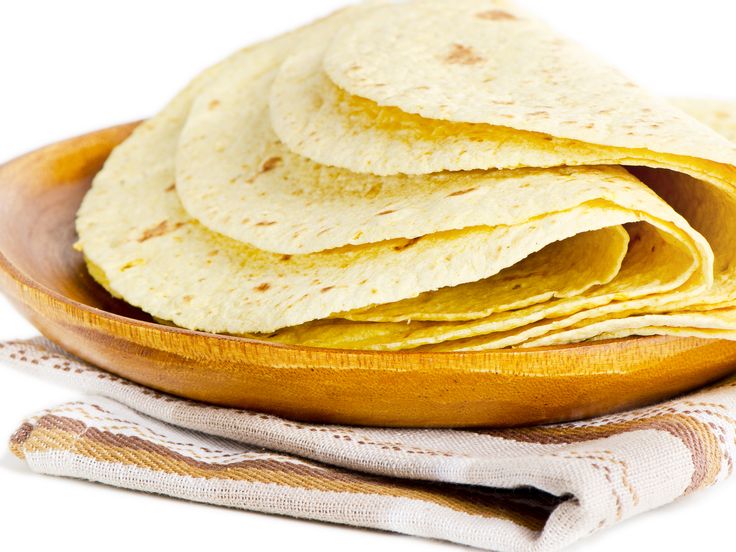 a wooden bowl filled with tortillas on top of a table