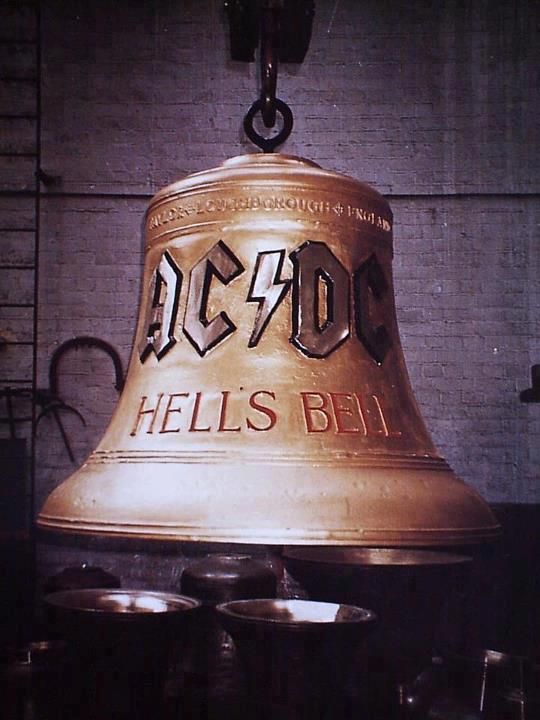 a large bell hanging from the side of a building with metal cups below it that reads ac dc hells bell