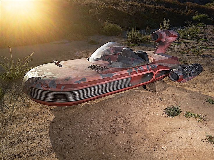 an old red car sitting in the middle of a dirt field with sun shining on it