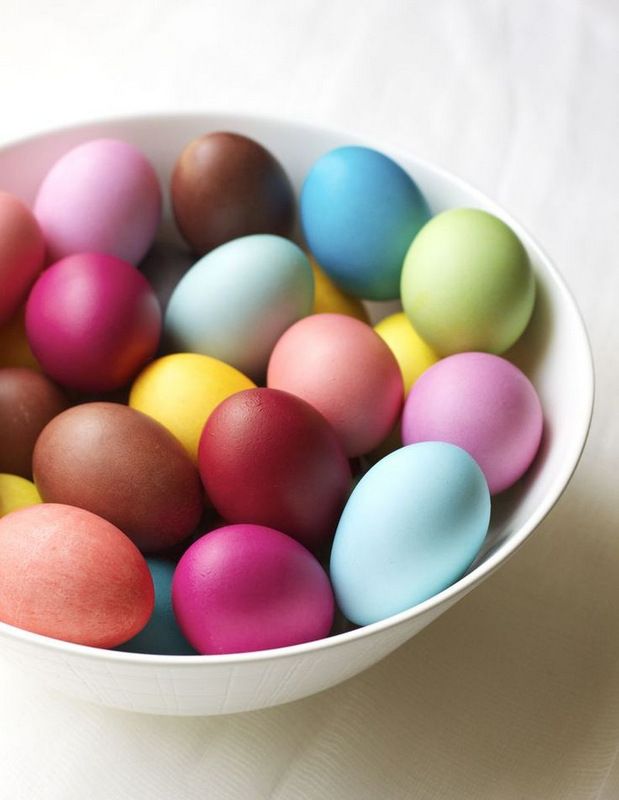 a white bowl filled with colorful eggs on top of a table