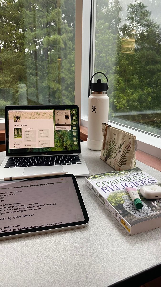 an open laptop computer sitting on top of a white desk next to a book and cup