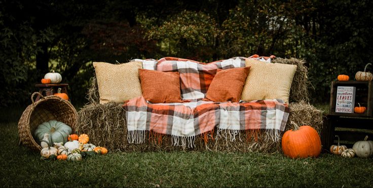 a hay bale with pumpkins and pillows on it in the grass next to a couch